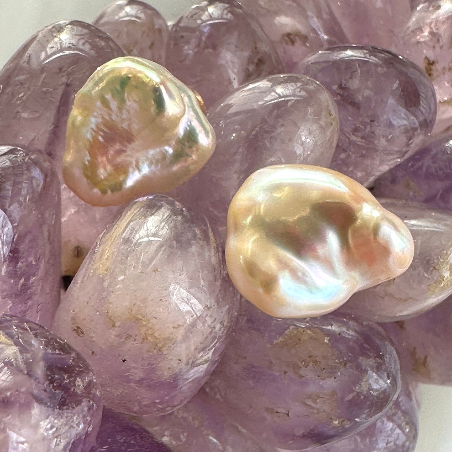 Champagne keshi pearl stud earrings placed beside amethyst crystal ornament, showing contrast of soft gold tones and gemstone color.