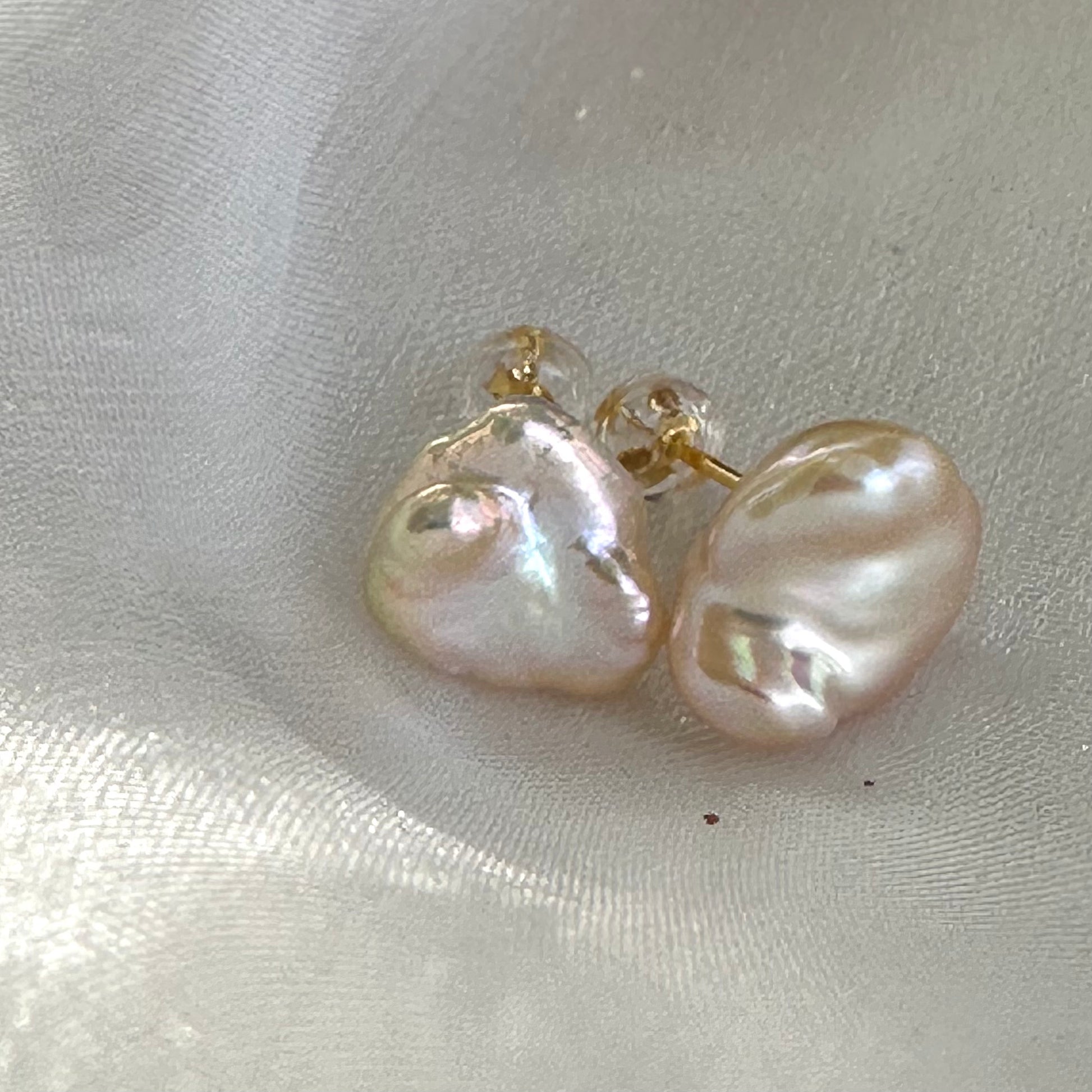 Elegant champagne keshi pearl stud earrings displayed on white shell, highlighting organic keshi shape and natural iridescence.