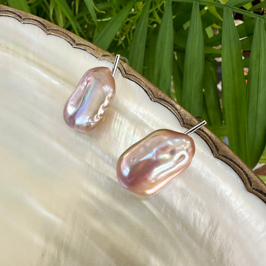 Rectangular purple pearl drop earrings on shell among greenery, highlighting iridescent tones and handcrafted sterling silver finish.