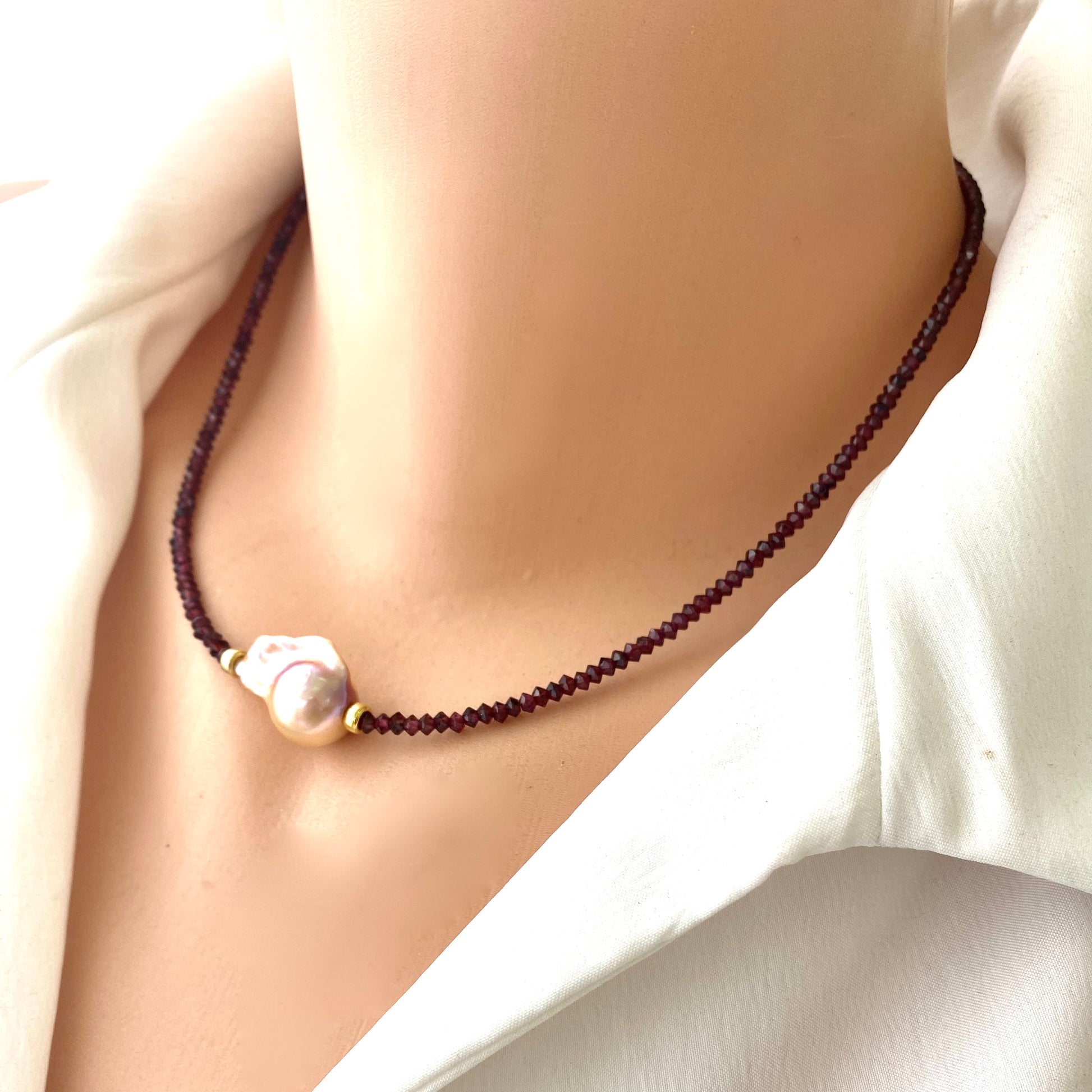 Red garnet baroque pearl necklace featuring a golden-pink pearl pendant on a person's neck.
