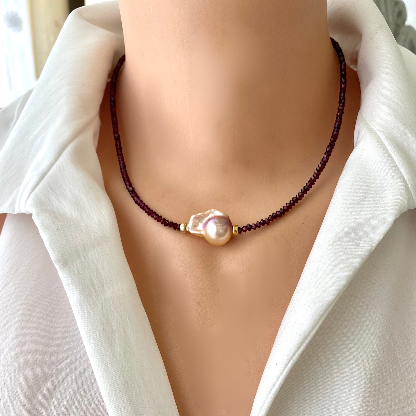 Red garnet baroque pearl necklace featuring a golden pink pearl pendant on a model's neck.