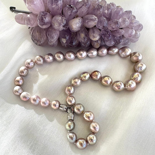 Pink lavender pearl necklace displayed on white cloth beside amethyst crystal ornament, showing elegant color contrast.