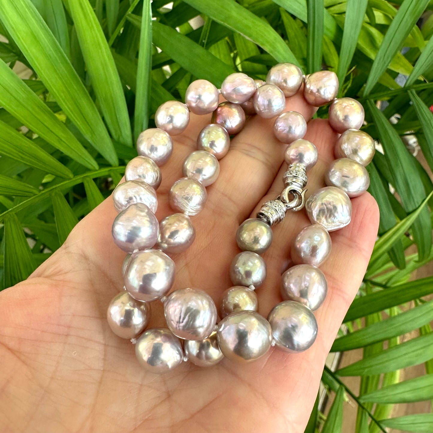 Pink lavender pearl necklace held in hand against green leaves, showing natural light reflection and organic luster.