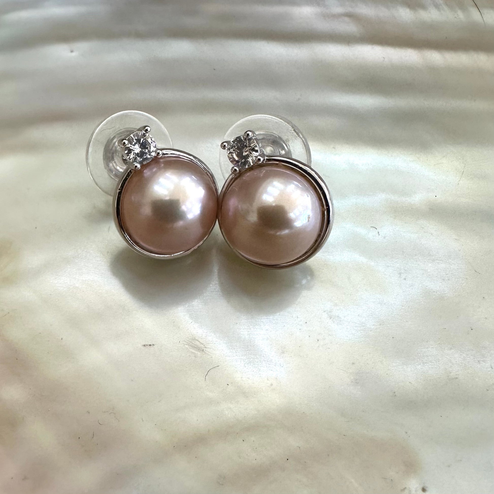 Pink mabe pearl stud earrings with cubic zirconia accent on white pearl shell, showing mirror-like sheen and smooth round pearls.