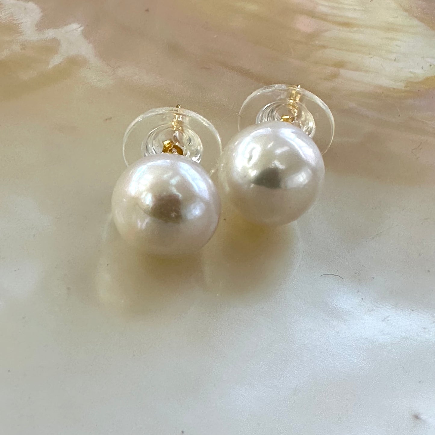 Elegant white edison pearl stud earrings displayed on white shell background, highlighting high luster and gold vermeil posts.