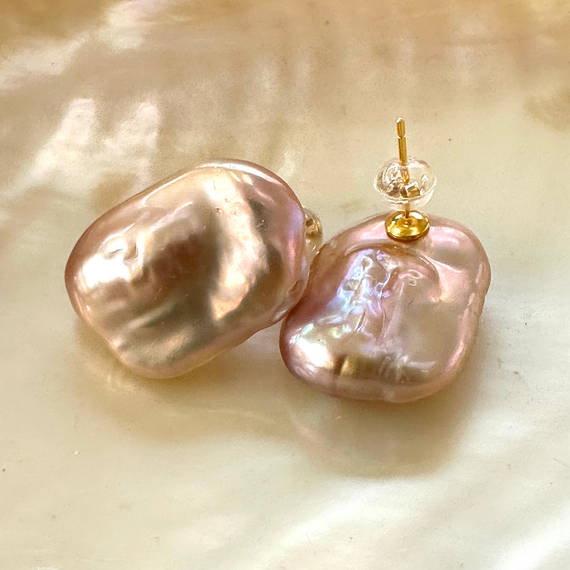 Golden pink rectangle baroque pearl stud earrings close-up on glowing yellow pearl surface, handmade in Canada.