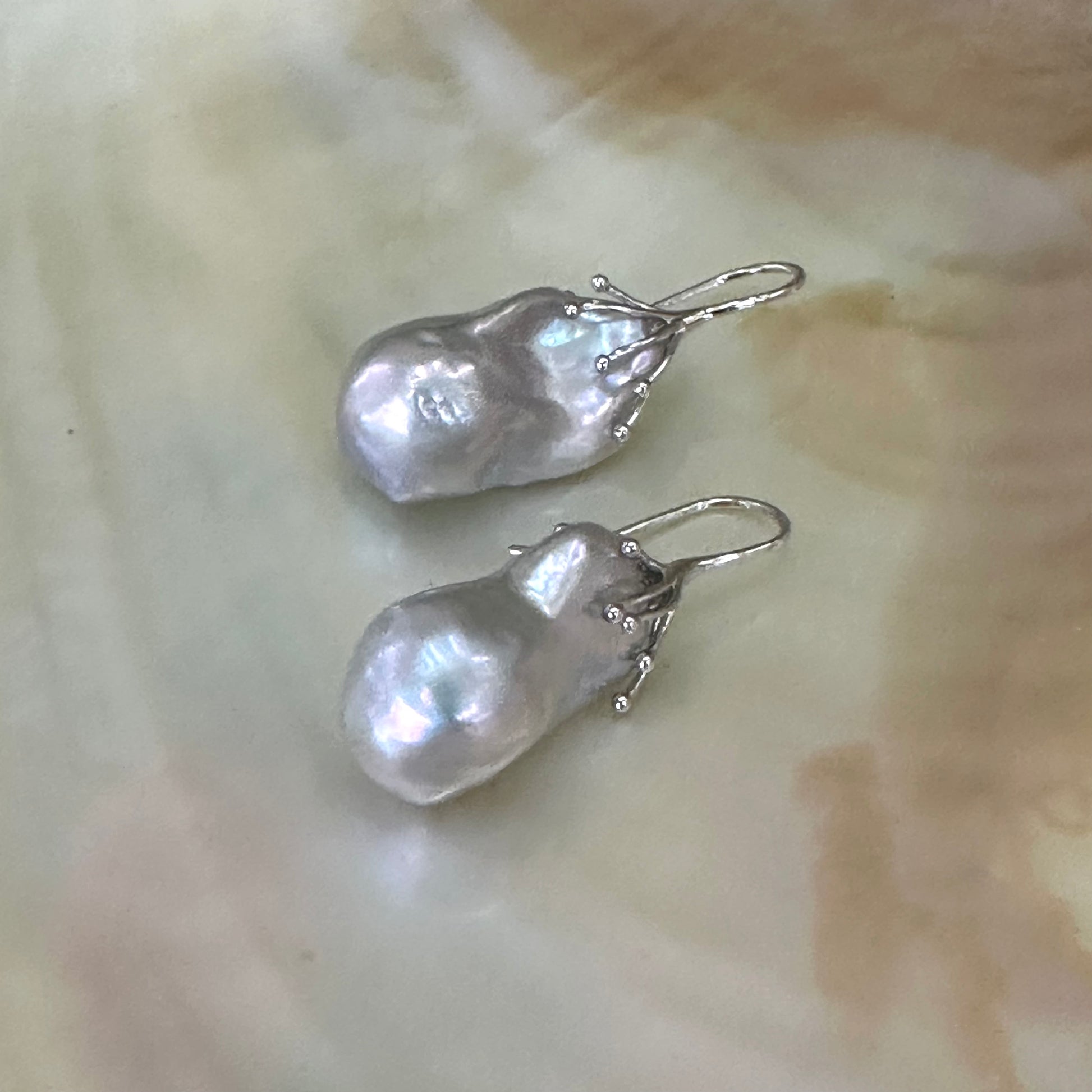 Silver grey baroque pearl drop earrings in sterling silver, close-up against white pearl shell backdrop showing lustrous surface.