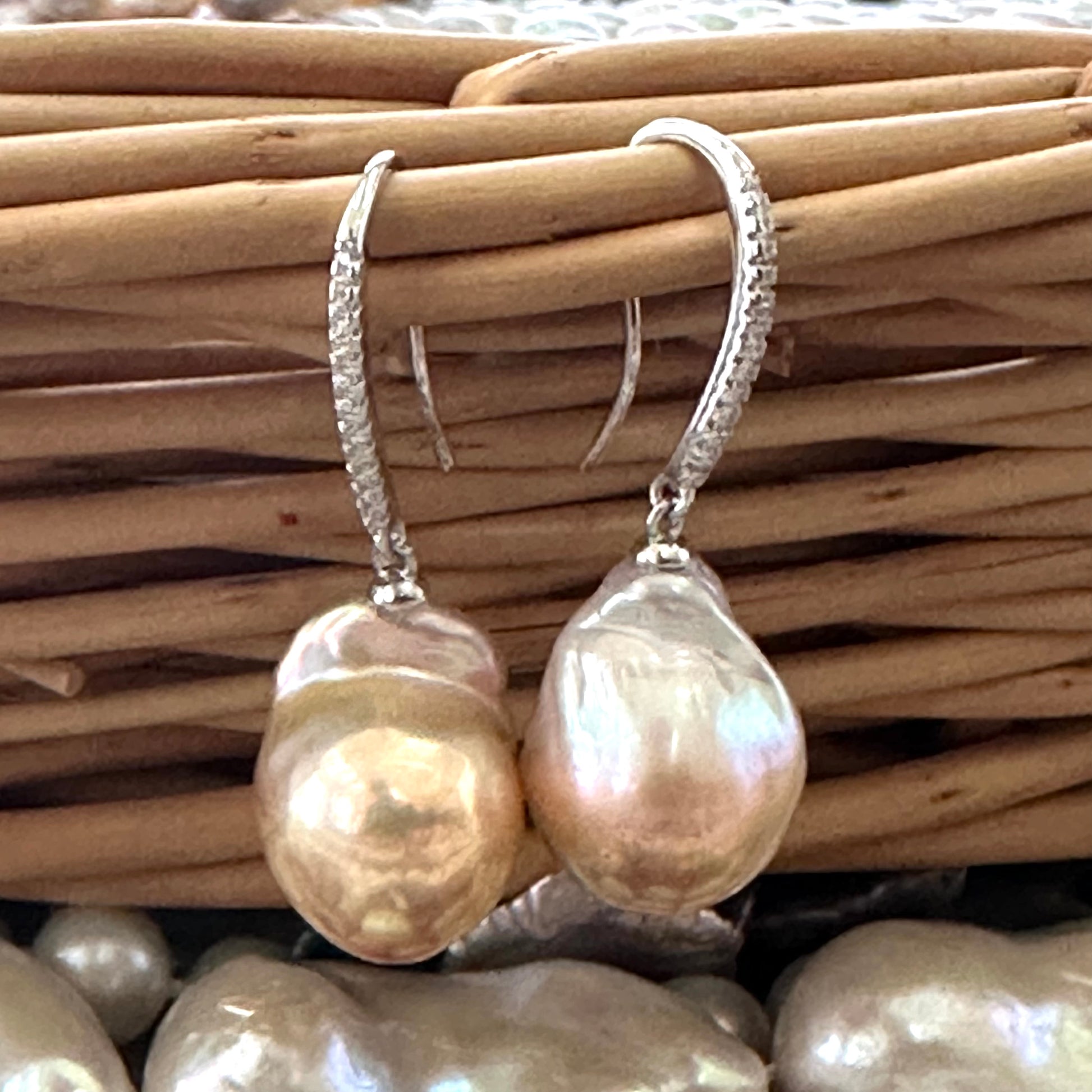 Golden pink baroque pearl dangle earrings resting on wicker basket, sterling silver CZ pavé design handmade in Canada.