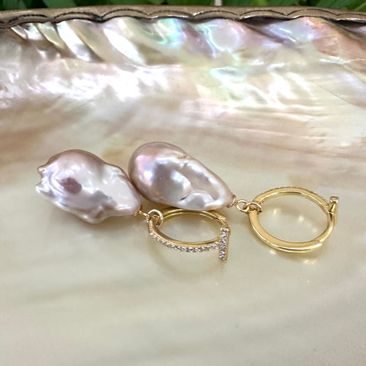 Pink baroque pearl hoop earrings resting on white pearl shell, designed and handmade in Canada.