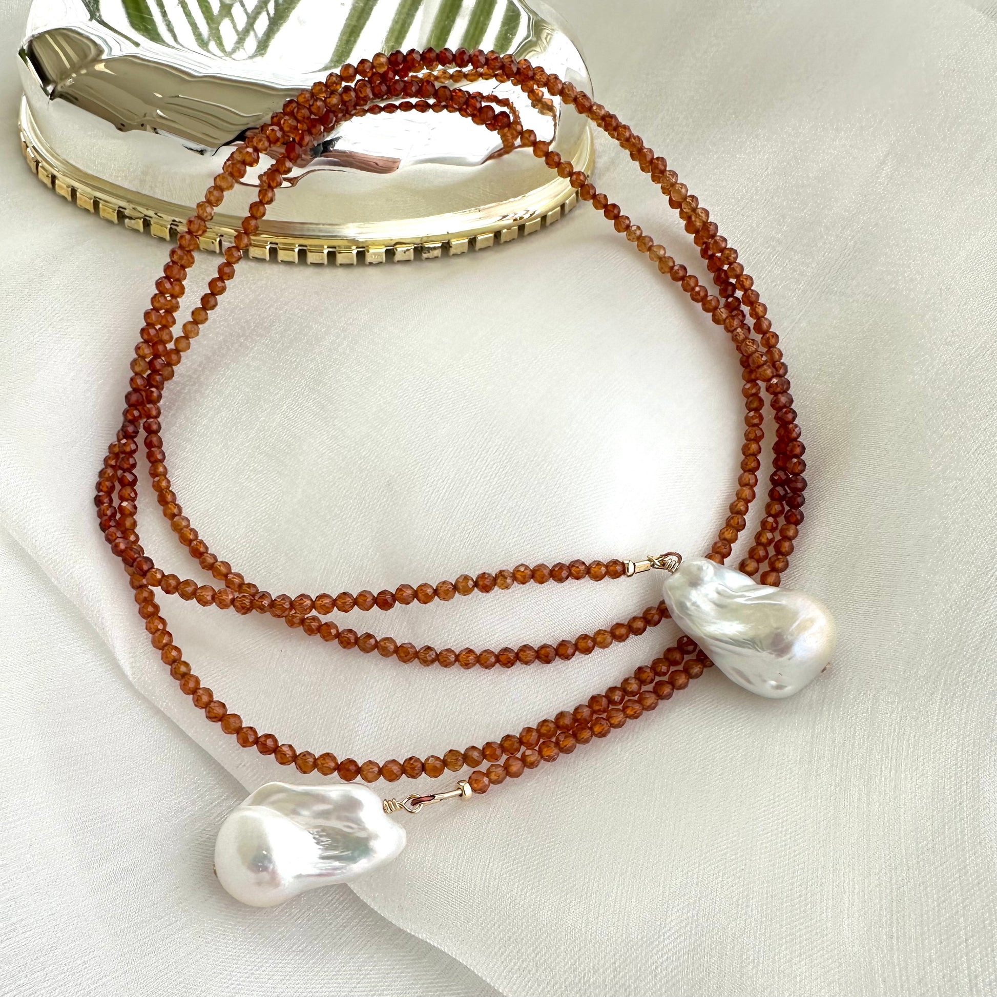 Hessonite Garnet and Baroque Pearl Lariat Necklace with gold-filled accents shown on white cloth background, designed and handmade in Canada.