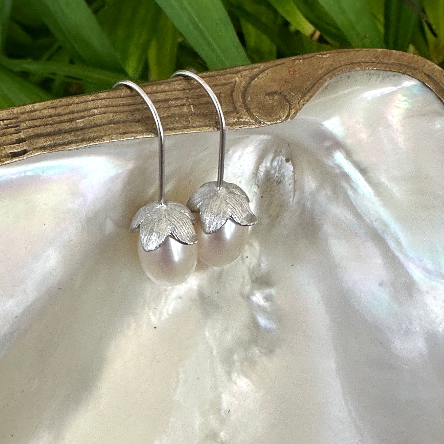 Rice Pearl Earrings – silver design displayed on pearl shell with green leaves