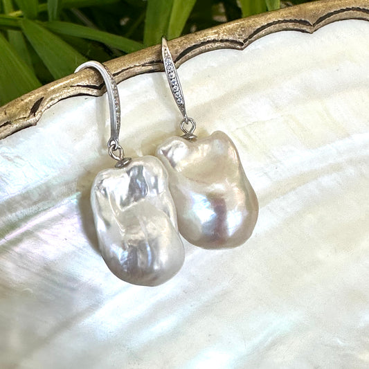 White baroque pearl bridal earrings resting on pearl shell and foliage background, handmade in Canada.