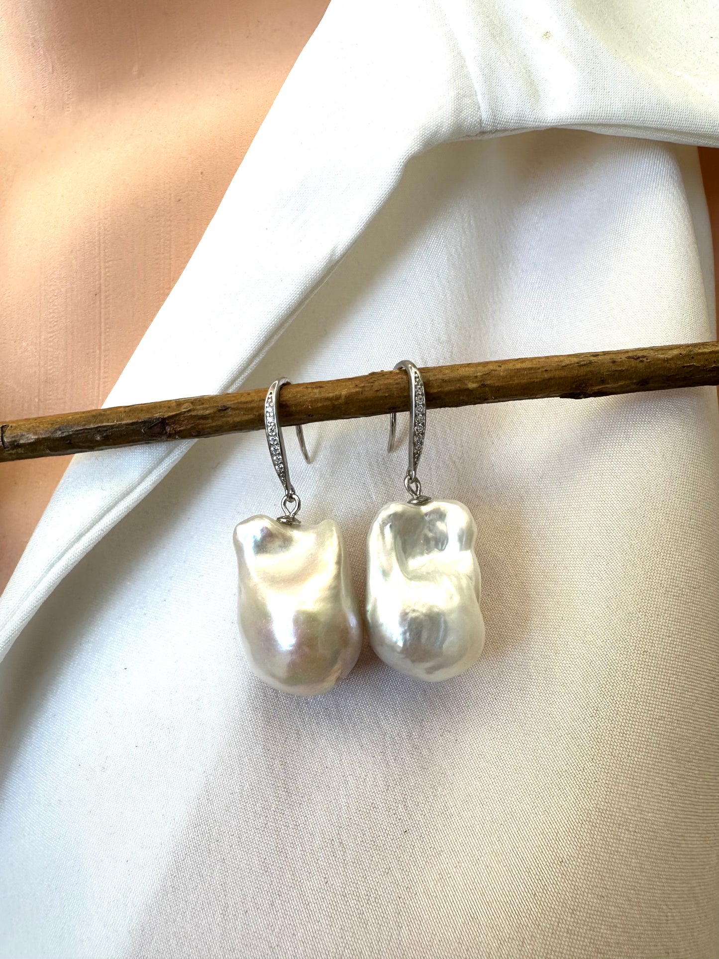 White baroque pearl bridal earrings hanging from branch in front of white blouse mannequin, designed and handmade in Canada.