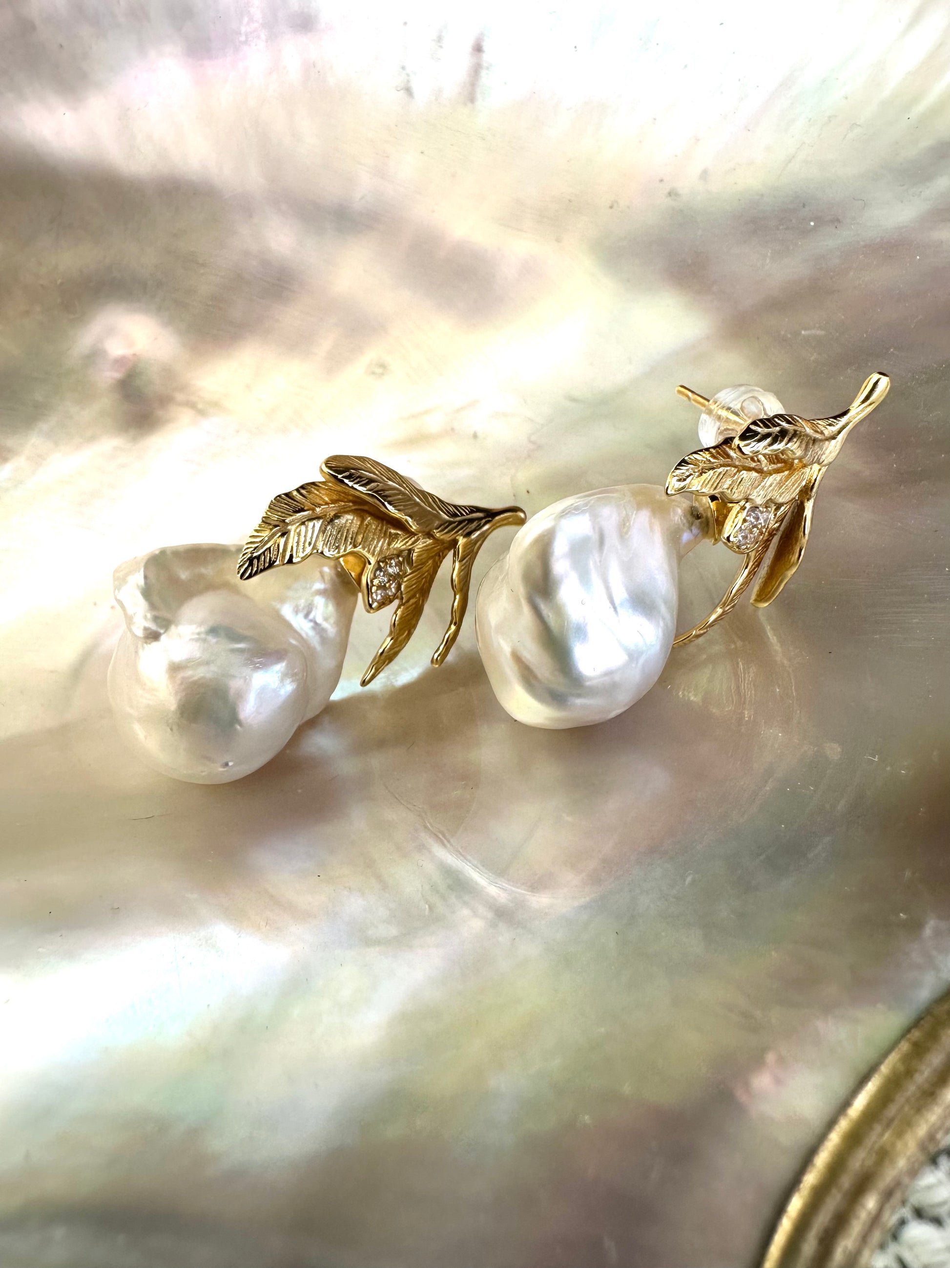 Close-up of handcrafted Baroque Pearl Earrings with oak leaf gold vermeil design displayed on white pearl shell background.