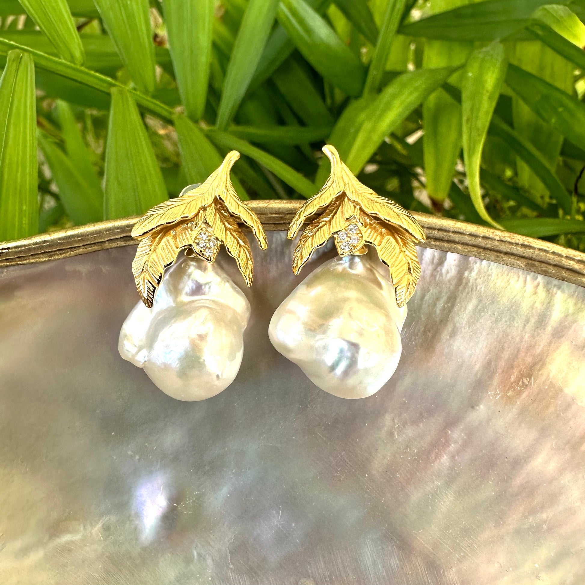 Nature-inspired Baroque Pearl Earrings with gold vermeil oak leaf design photographed on white shell and green leaf background.
