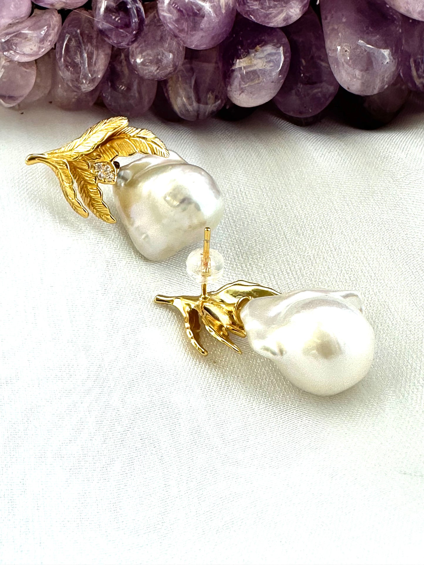 Baroque Pearl Earrings with gold vermeil oak leaf accents displayed beside raw amethyst gemstone on white backdrop.
