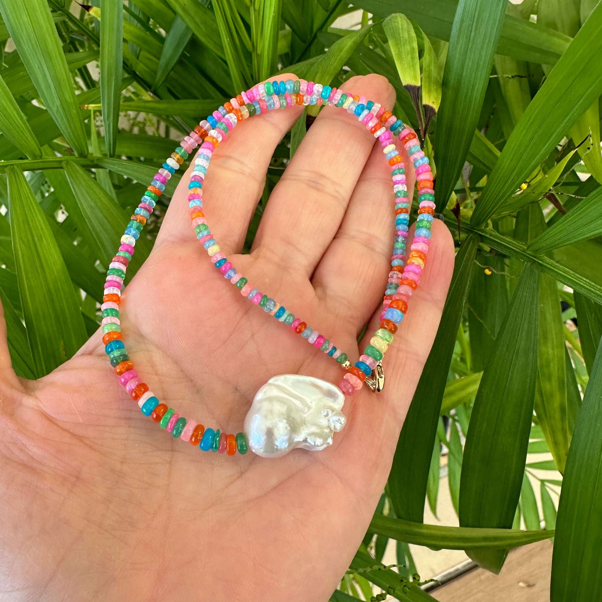 Close-up of opal and baroque pearl necklace in natural light against leaves
