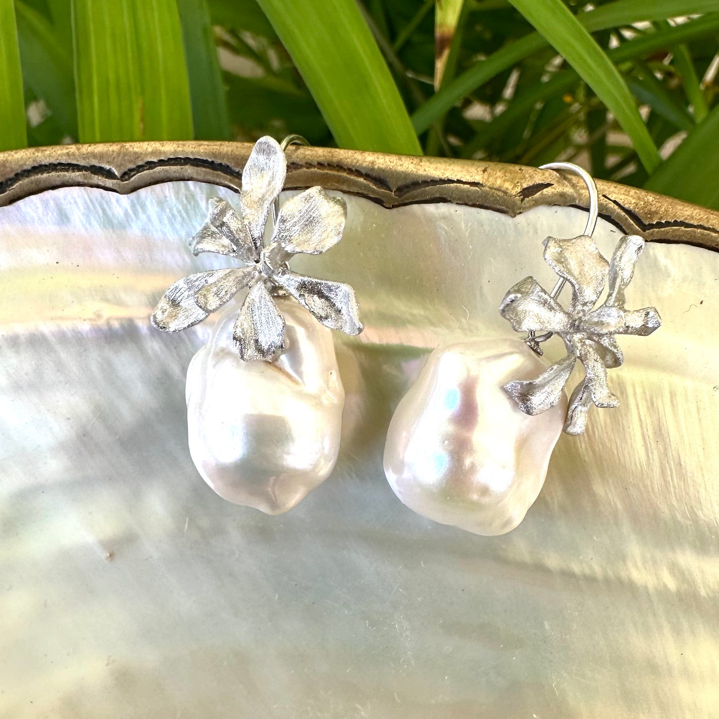 Silver baroque pearl drop earrings on white pearl and green leaf background