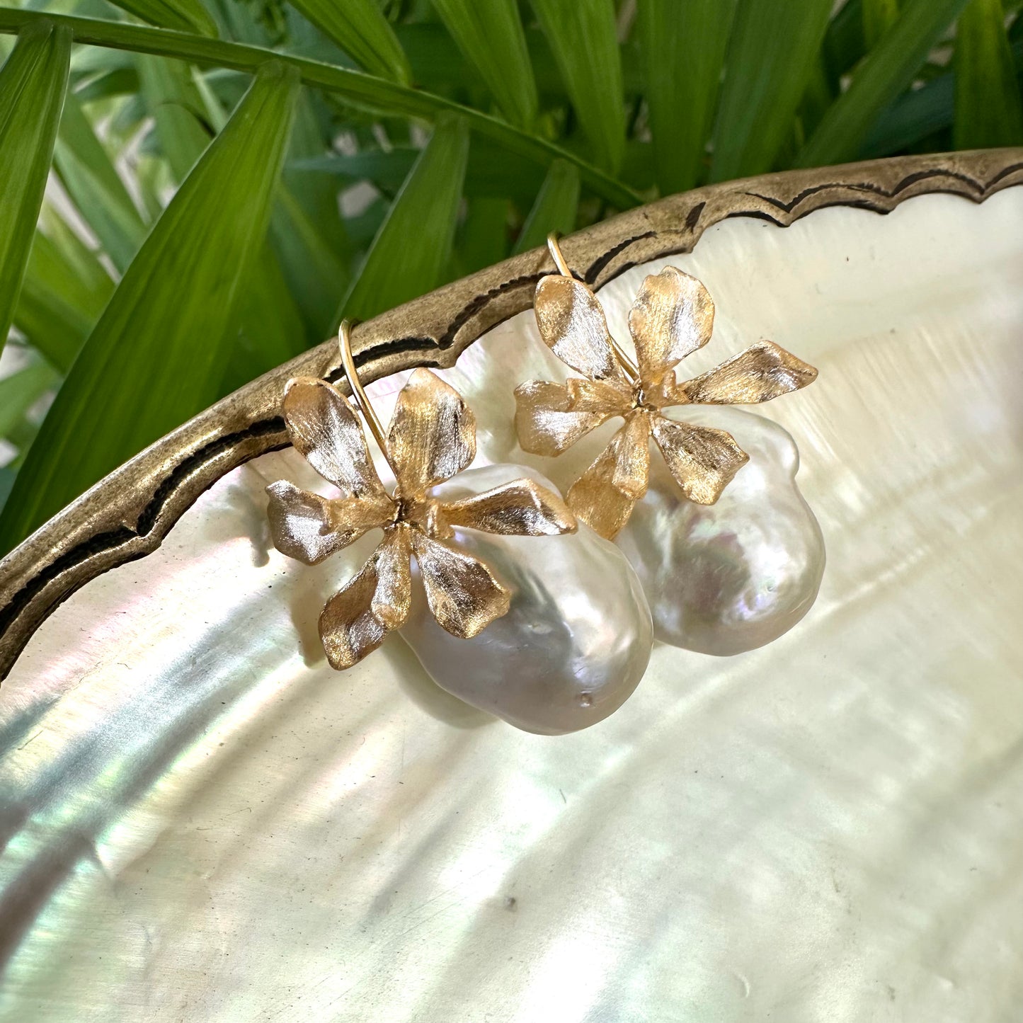 Gold baroque pearl drop earrings with flower design on white and green backdrop