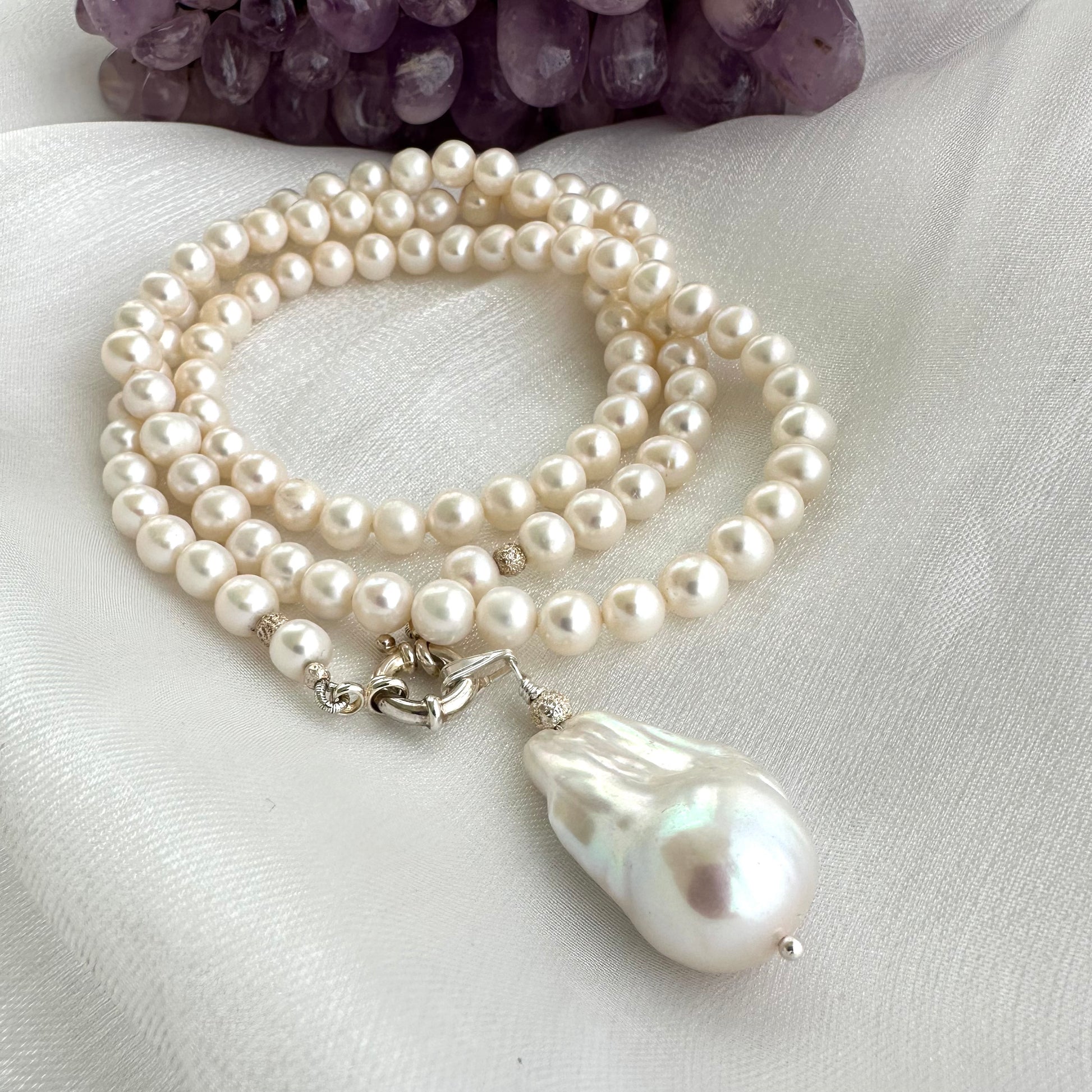 Close-up of white pearl necklace with baroque pendant on white background