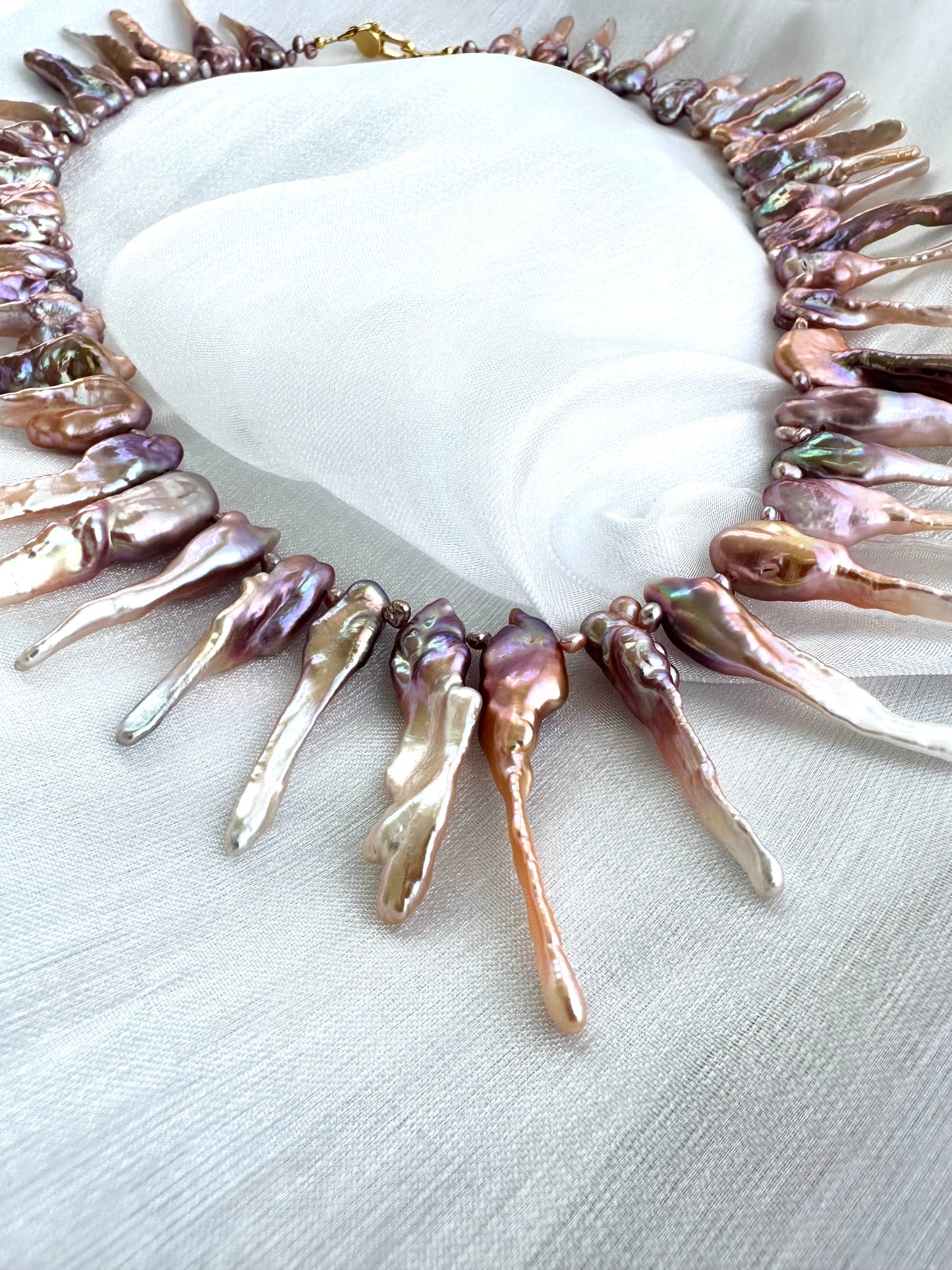 Detailed view of pink Biwa pearl necklace pearls and gold clasp on white fabric