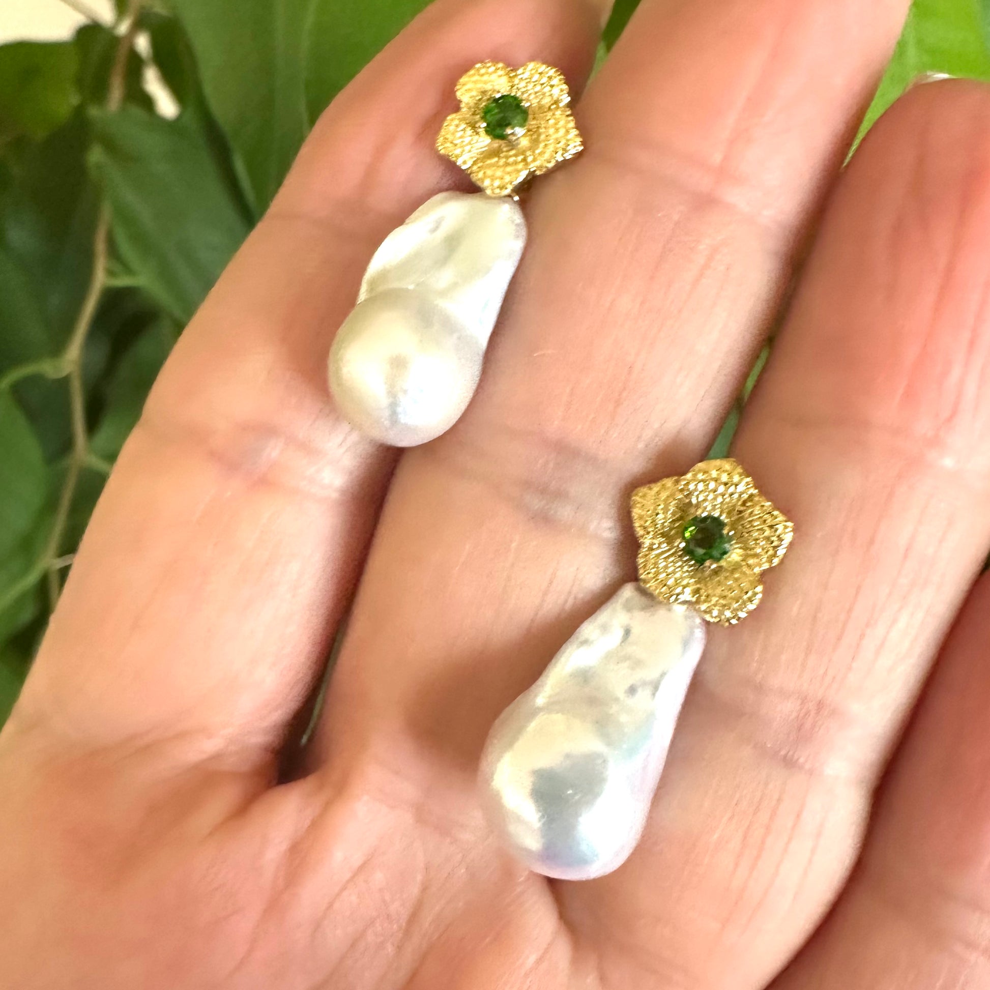 Handmade chrome diopside pearl earrings with removable baroque drops, shown in hand against green leaf