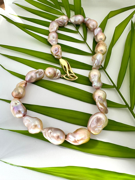 Close view of golden pink baroque pearl necklace against green leaf backdrop