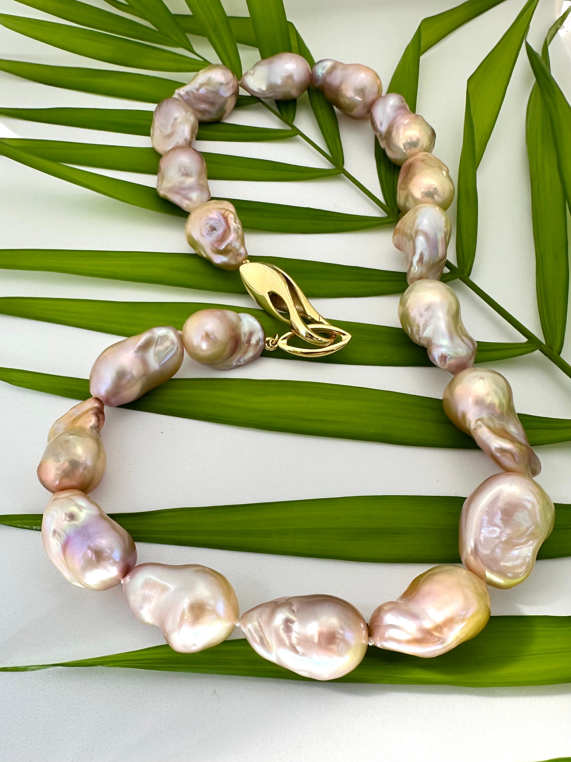 Golden pink baroque pearl necklace detail on green leaf background, natural light