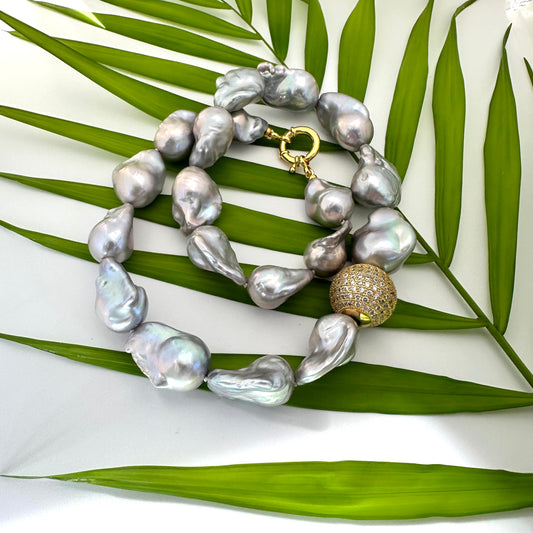 Silver grey baroque pearl necklace close up on green leaf background