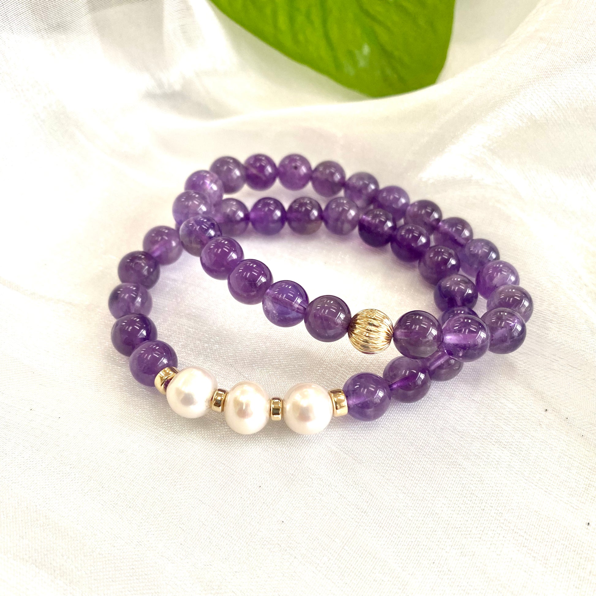 Amethyst Pearl Bracelet pair on white cloth – one with three pearls and one without