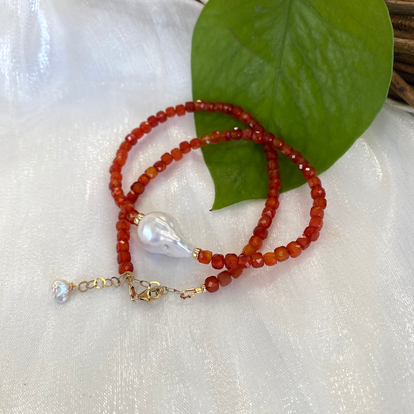 Carnelian pearl necklace with burnt orange carnelian beads and a white pearl pendant on a soft fabric background.