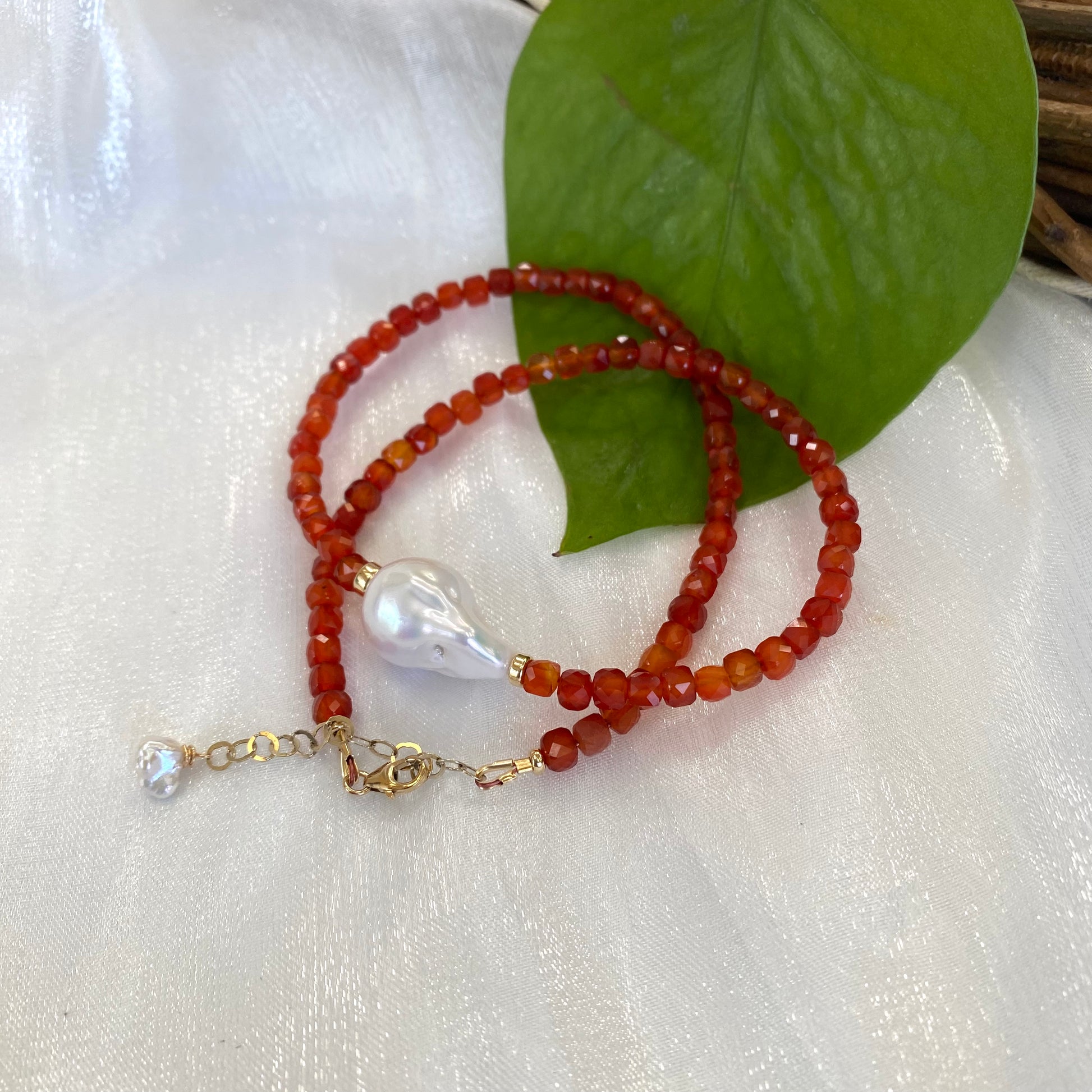 Carnelian pearl necklace with burnt orange carnelian beads and a white pearl pendant on a soft fabric background.
