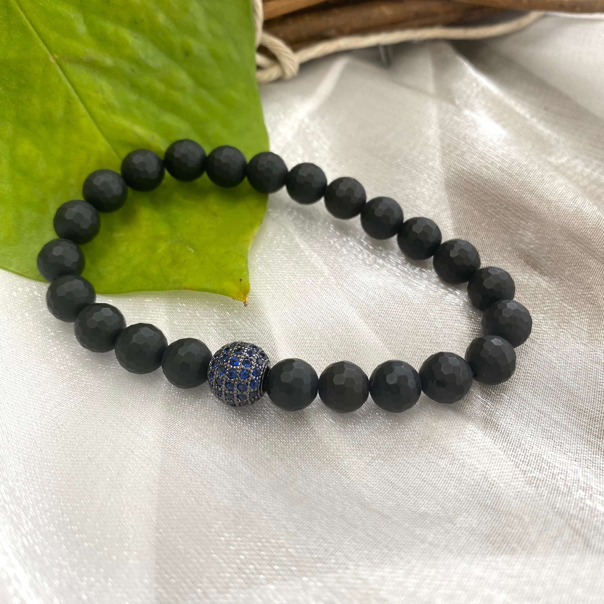 Matte black onyx mens bracelet featuring blue CZ centerpiece on a textured surface.
