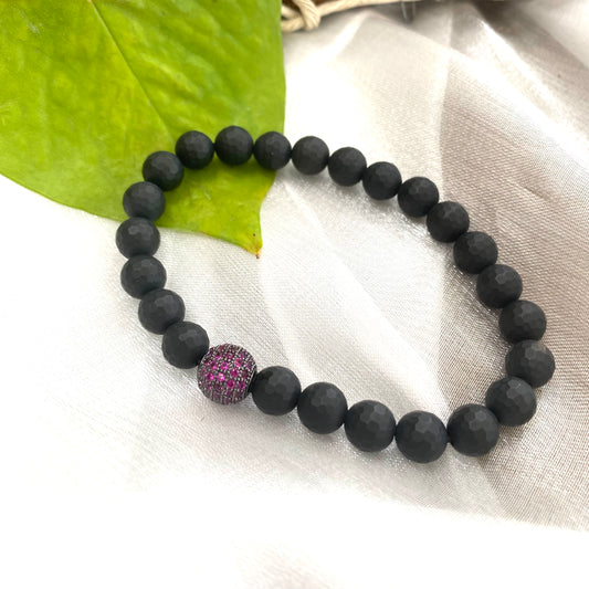 Matte black onyx mens bracelet featuring ruby red CZ spacer, stylish stretch design on a soft surface.