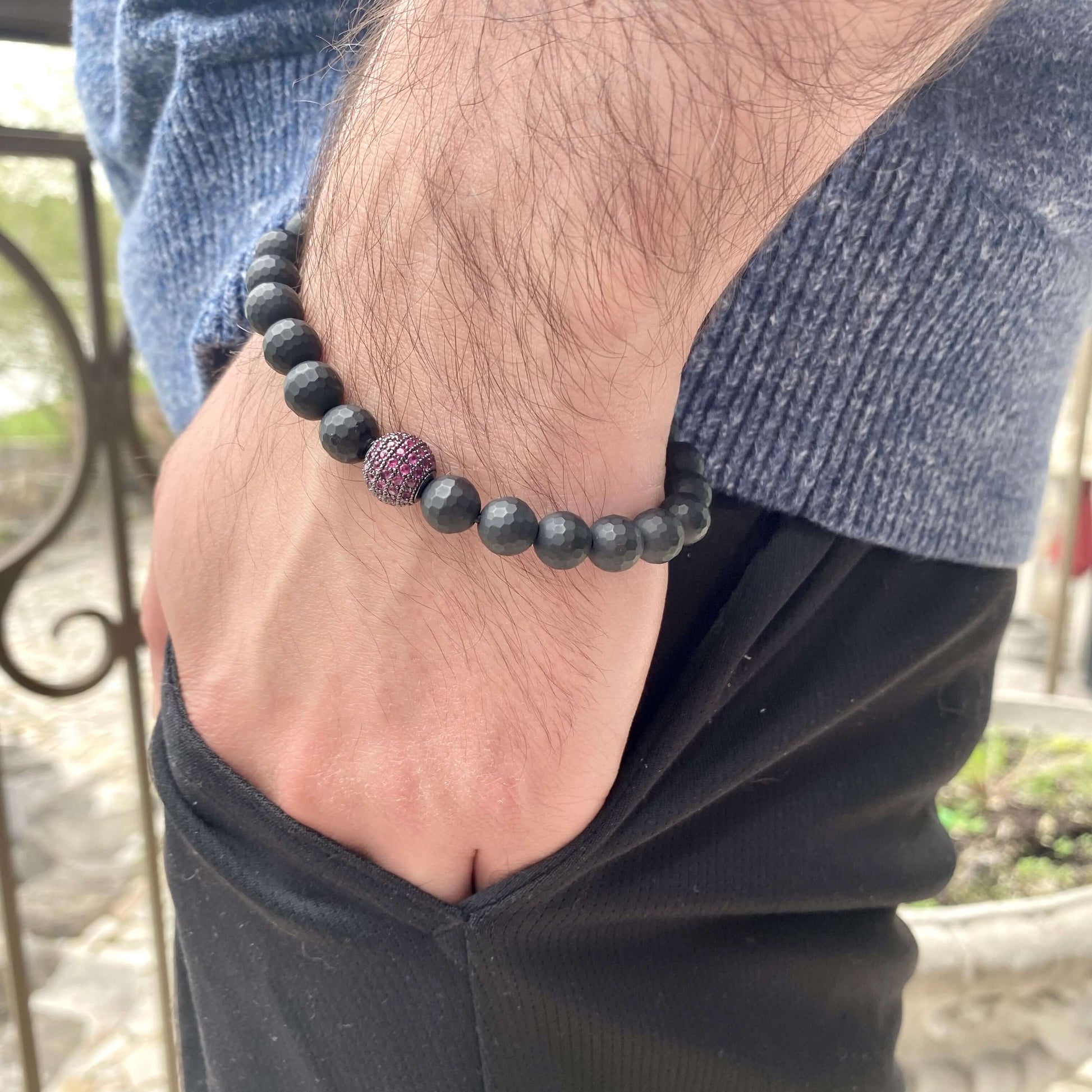 Matte black onyx mens bracelet worn on wrist, featuring a ruby red CZ spacer and faceted black onyx beads.