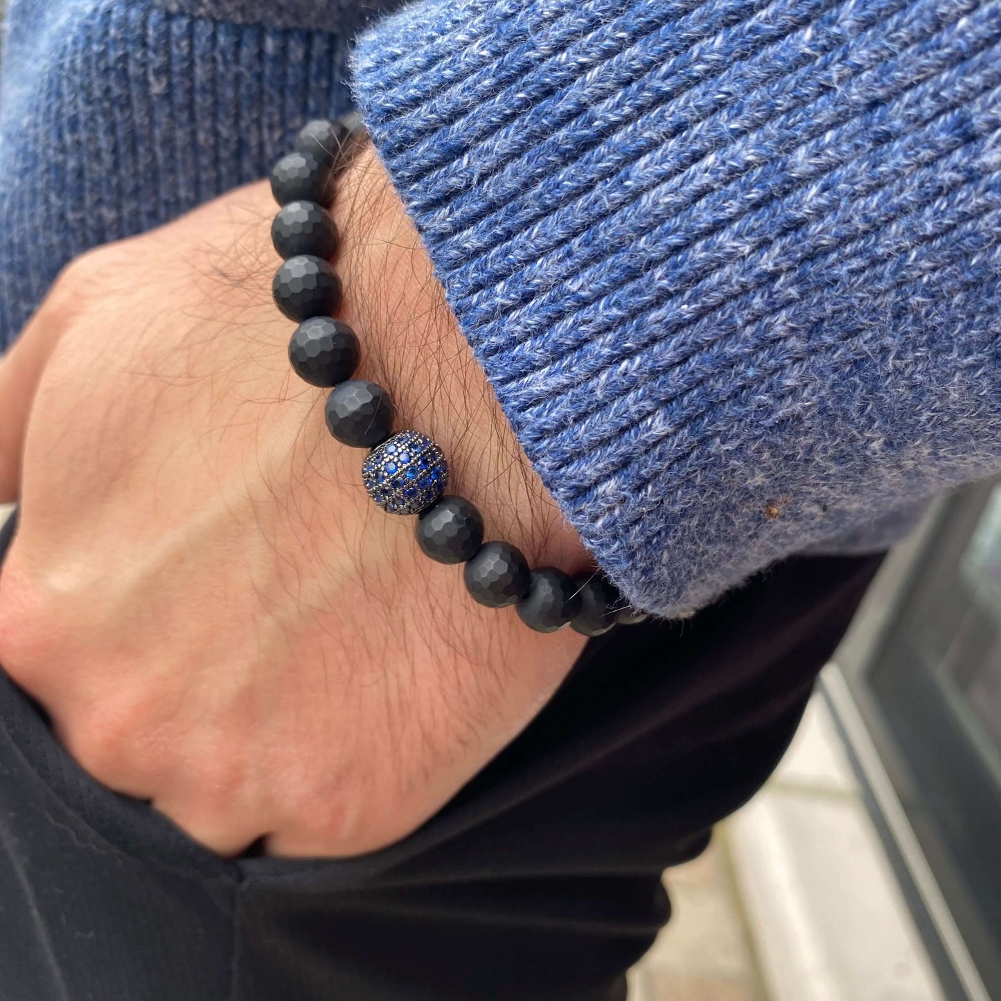 Matte black onyx mens bracelet with blue CZ, worn on wrist, showcasing stylish stretch design.