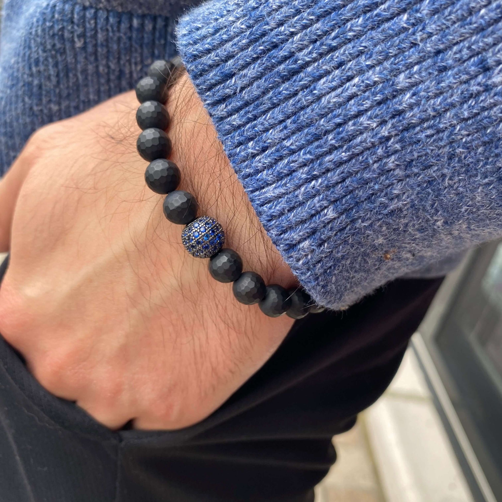 Matte black onyx mens bracelet with blue CZ, worn on wrist, showcasing stylish stretch design.