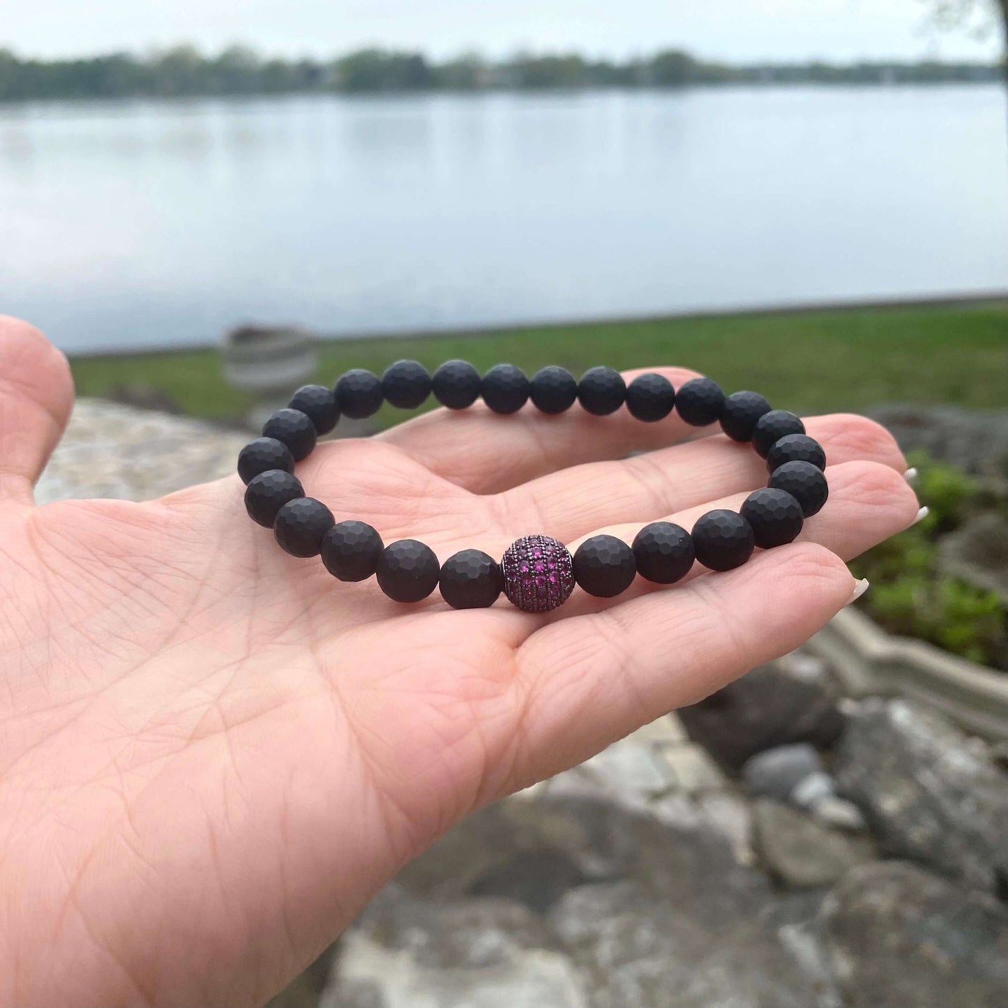 Matte black onyx mens bracelet displayed on hand, featuring ruby red CZ accent, perfect for modern style.