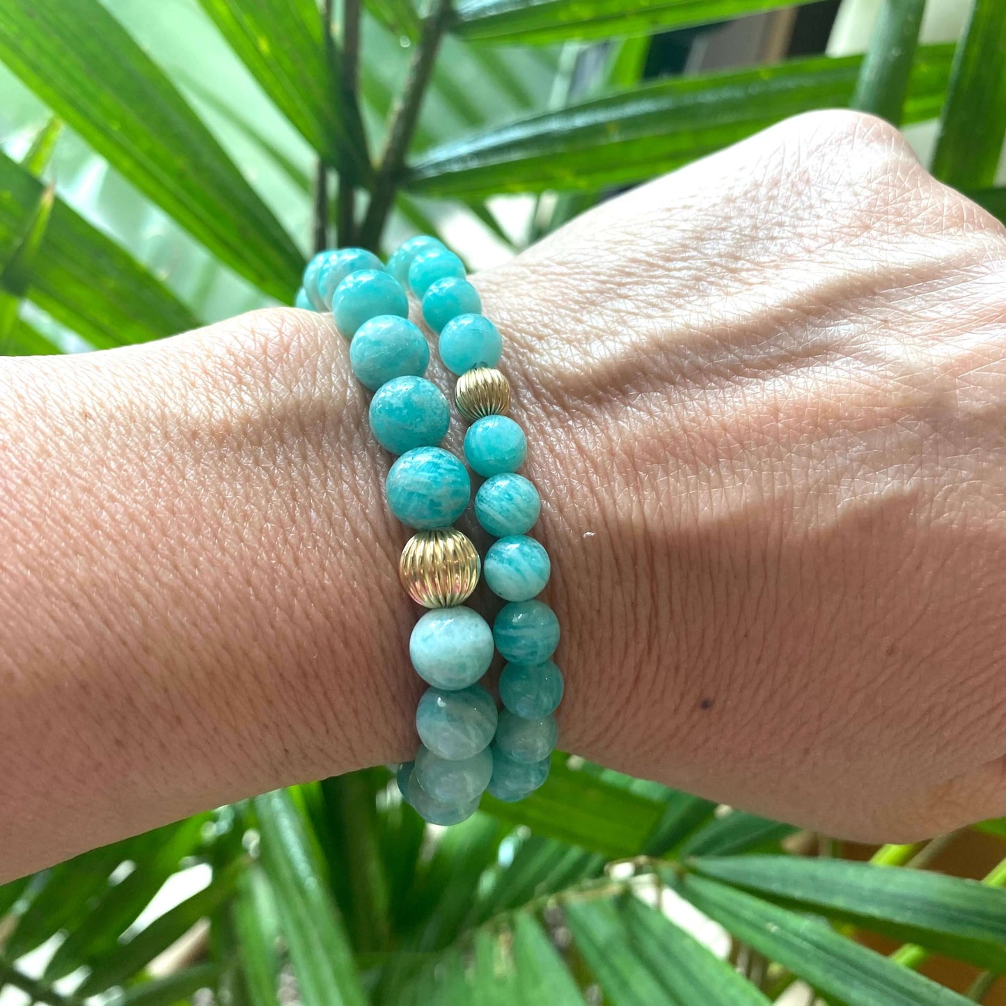 Green Amazonite Stretch Bracelet – 6mm or 8mm, 14K Gold Filled worn on wrist surrounded by green plant leaves.