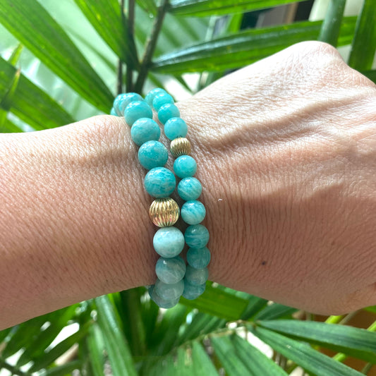 Green Amazonite Stretch Bracelet – 6mm or 8mm, 14K Gold Filled worn on wrist surrounded by green plant leaves.