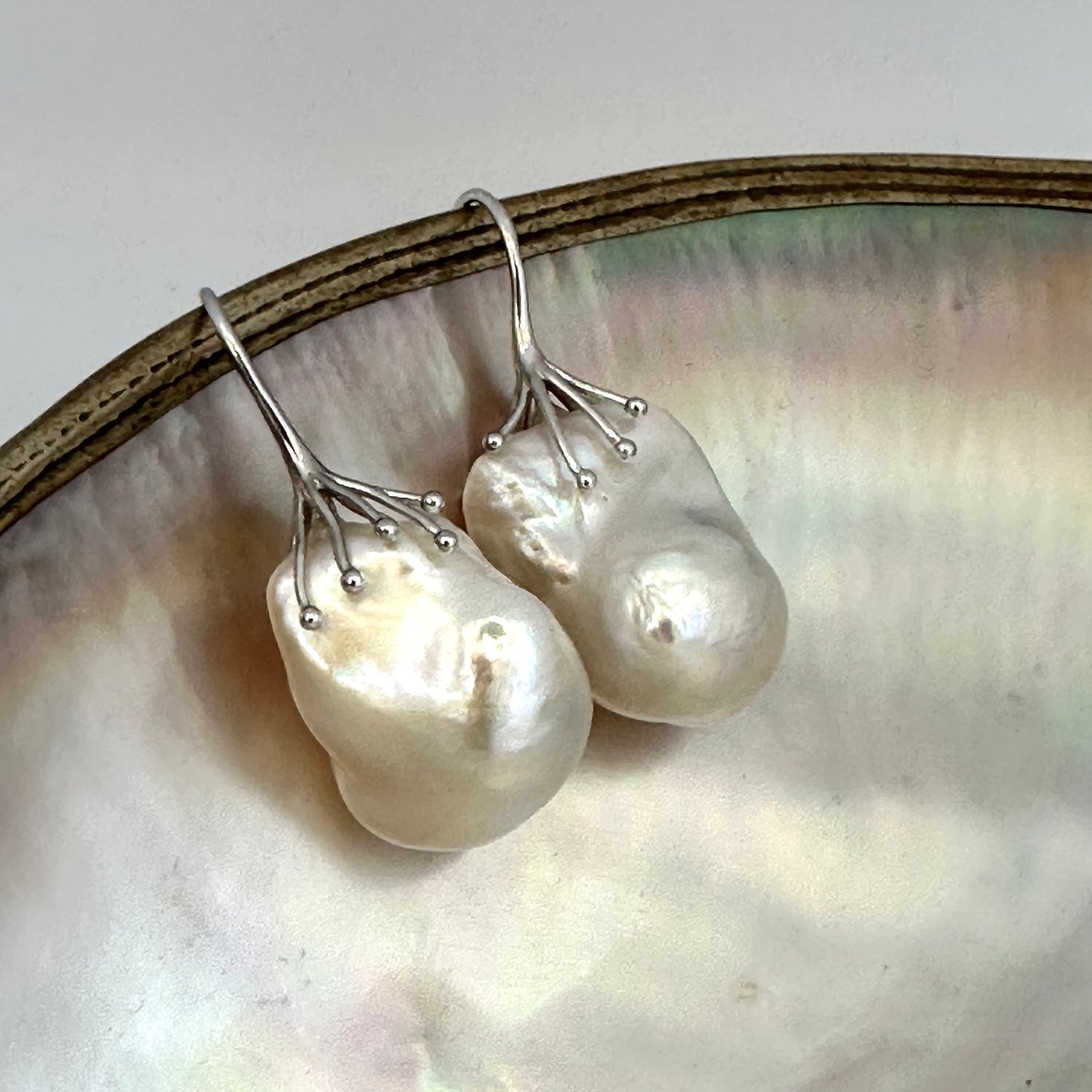 Baroque pearl drop earrings photographed on white pearl background – silver finish