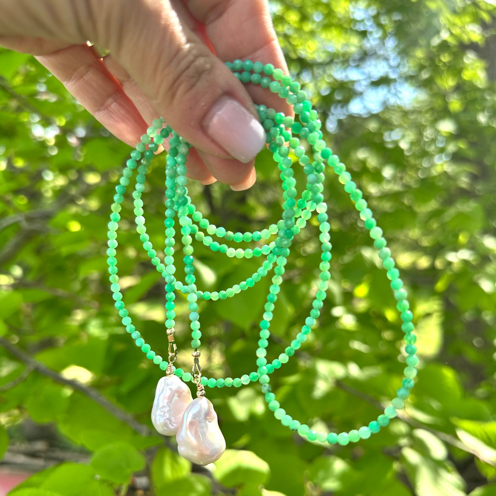 Apple Green Chrysoprase Lariat Necklace held against green leaves — natural gemstone and pearl lariat handcrafted by Loulia Pearl Jewelry