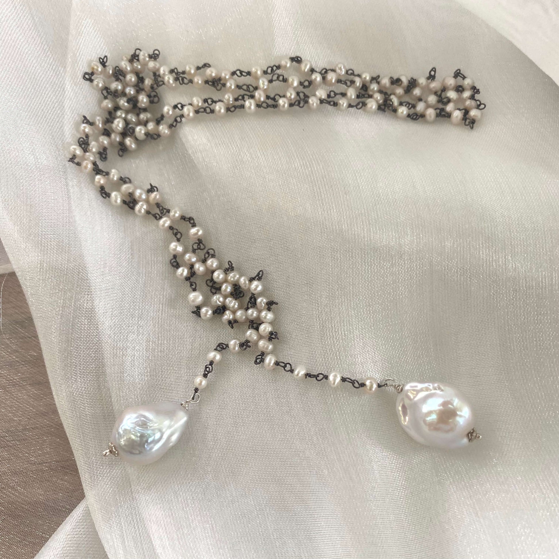 Pearl lariat rosary chain necklace displayed on white cloth background highlighting elegant design