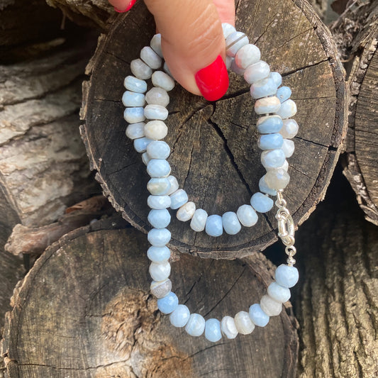 Blue grey opal necklace held in hand against wood logs backdrop