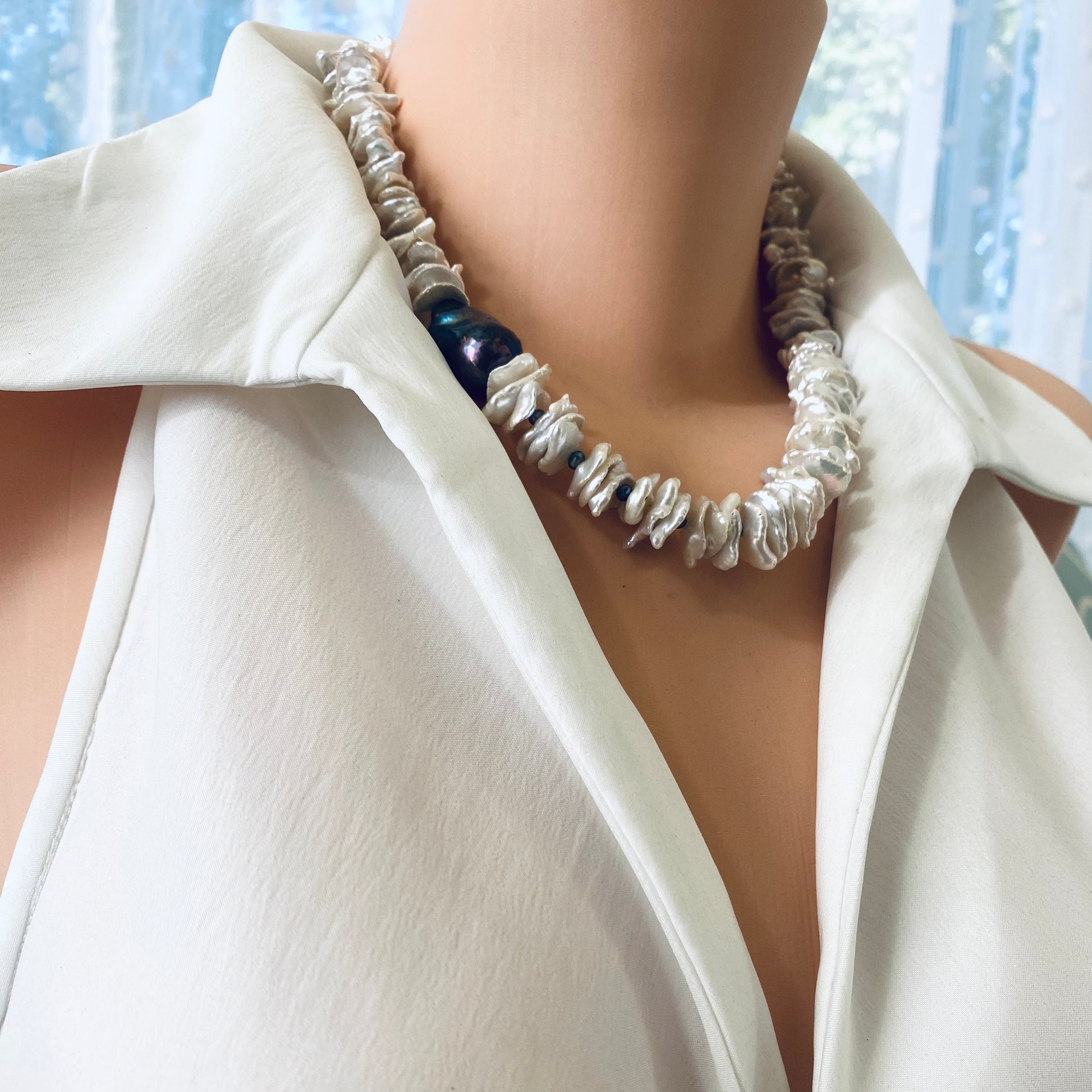 White cornflake pearl necklace with a black baroque pearl pendant elegantly draped on a mannequin.