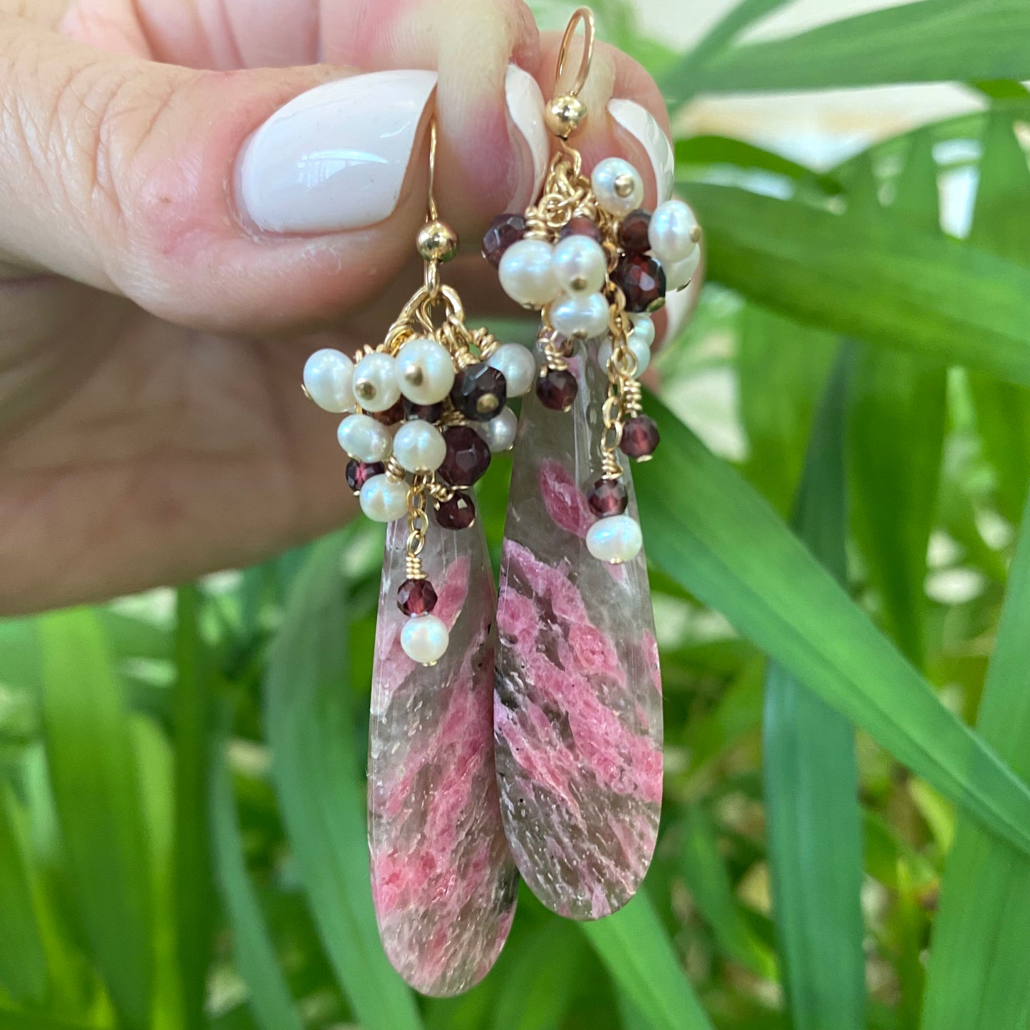 Pink rhodonite teardrop earrings detailed view in natural green foliage handmade in Canada