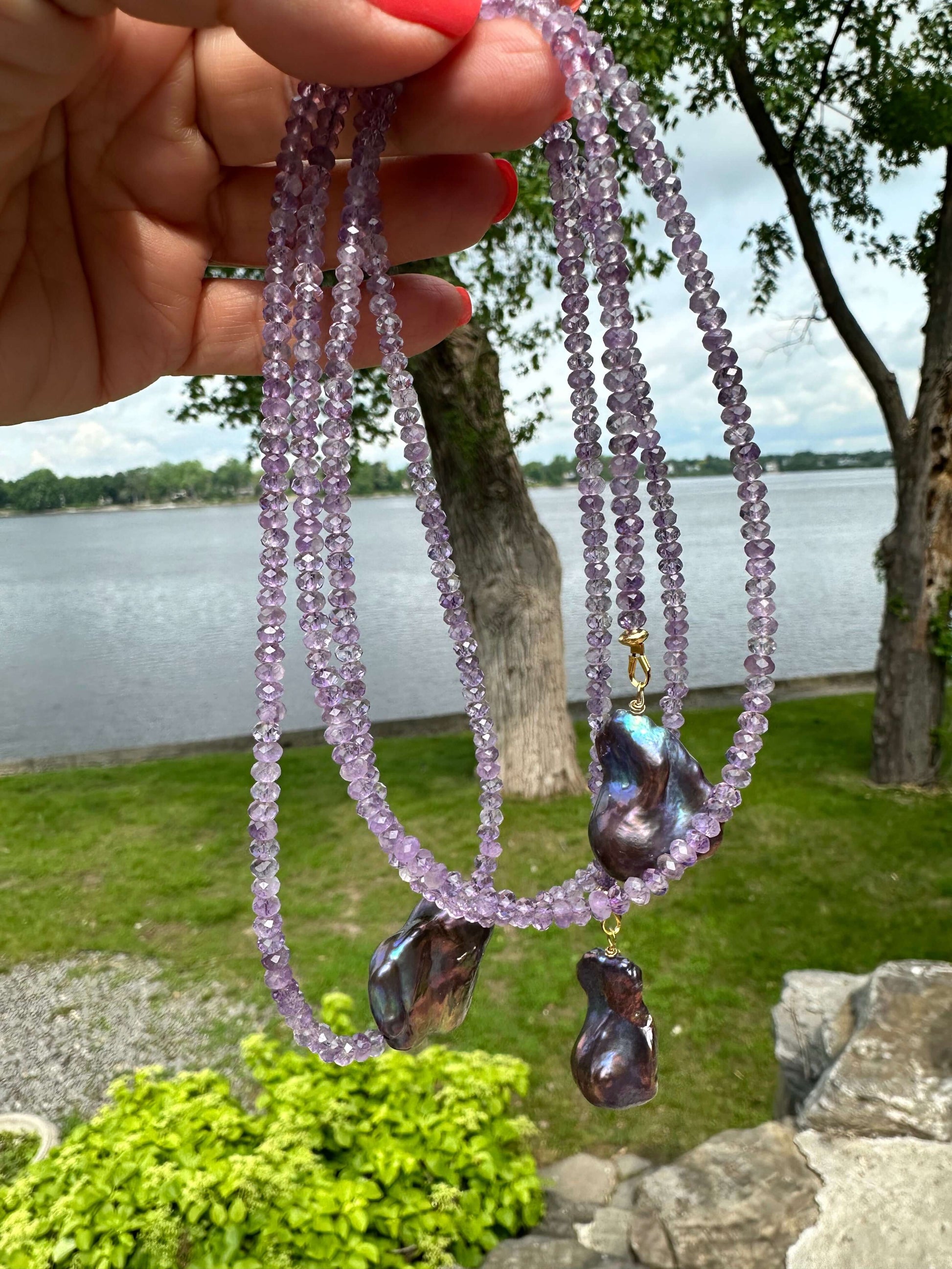 Amethyst and Black Baroque Pearl Lariat Necklace held outdoors against lake and grass background — natural gemstone jewelry by Loulia Pearl Jewelry
