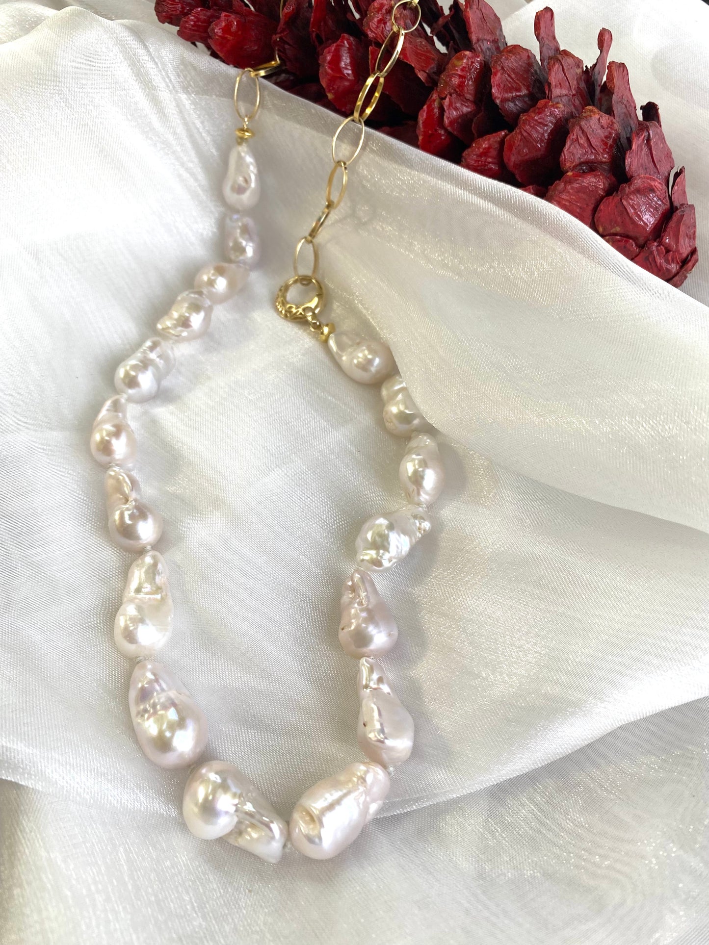 White baroque pearl and gold chain necklace detailed view on white cloth beside pine cone, designed and handmade in Canada.