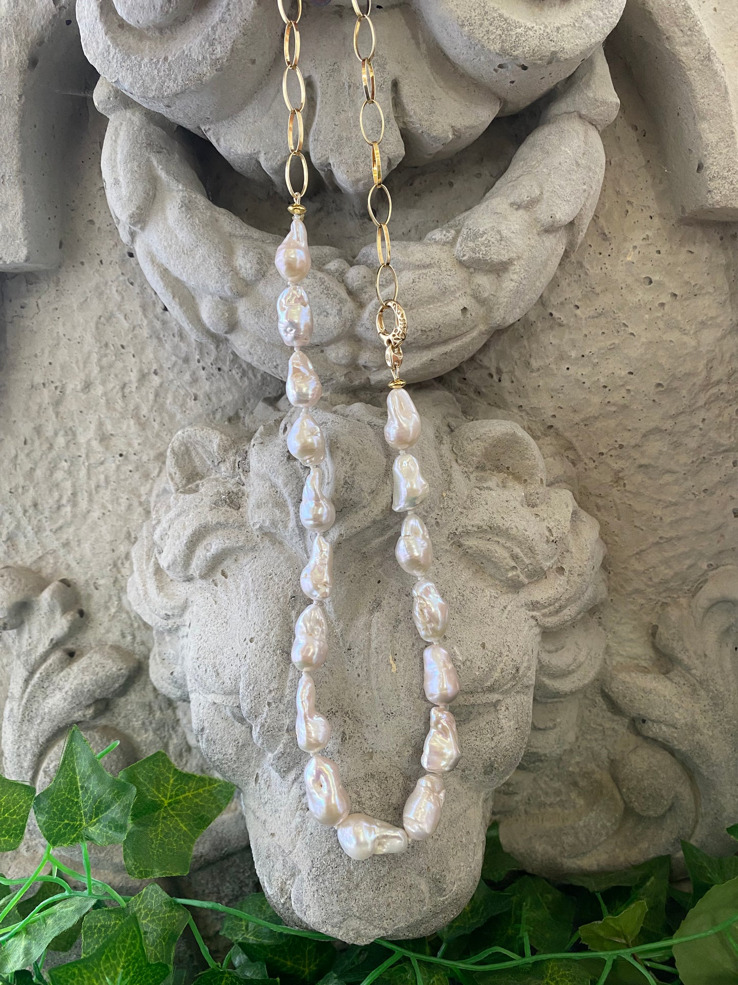 White baroque pearl and gold chain necklace draped from cement statue, modern asymmetric handmade necklace from Canada.