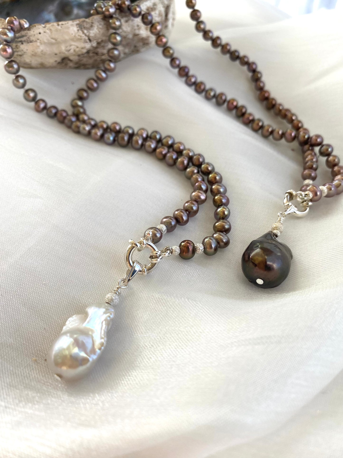 White and brown baroque pendant bronze pearl necklaces side by side on white cloth, showing variant colors and handmade quality.